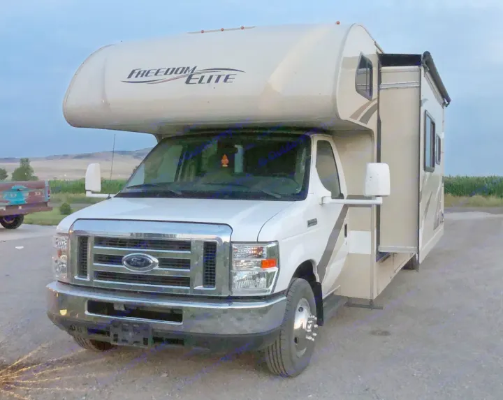 White Ford Freedom Elite Class C RV rental, slide-out extended, parked on gravel. Ideal for travel and camping.. Thor Freedom Elite 2017