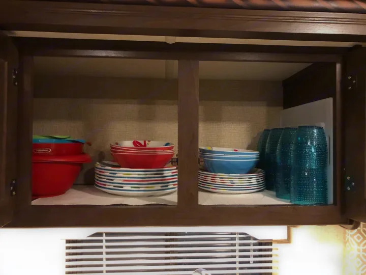 Inside an RV rental, an organized cabinet holds colorful dishes & blue glasses, ready for your adventure's meals.. Thor Freedom Elite 2017