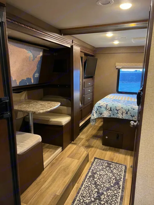 RV rental interior featuring a dinette with a map, a bed with patterned comforter, and storage with TV.. Thor Freedom Elite 2017