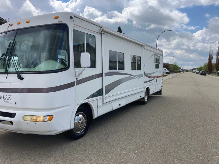 Explore with this Class A Daybreak RV rental, seen parked on a quiet residential street on a cloudy day.. Damon Corporation Daybreak 2002
