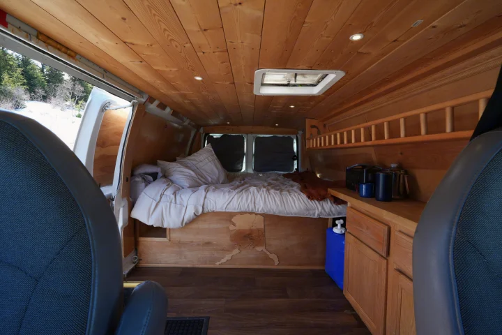 Experience a unique RV rental: a custom wood-paneled camper van interior with a bed, counter, and scenic snowy views.. Ford E250 Camper Van 2001