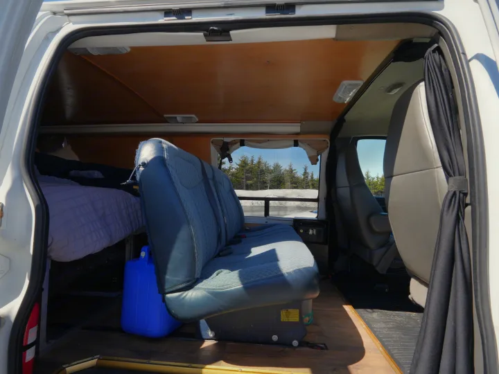 Inside a spacious RV rental camper van, featuring a comfortable bed, rear bench seat, and scenic winter window view.. Chevrolet Other 2006