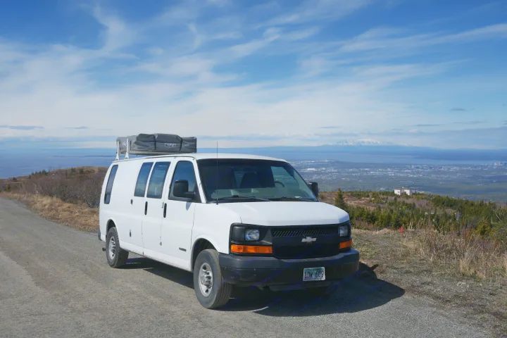 White RV rental van with rooftop tent on a scenic Alaska mountain road, overlooking the city and mountains.. Chevrolet Other 2006