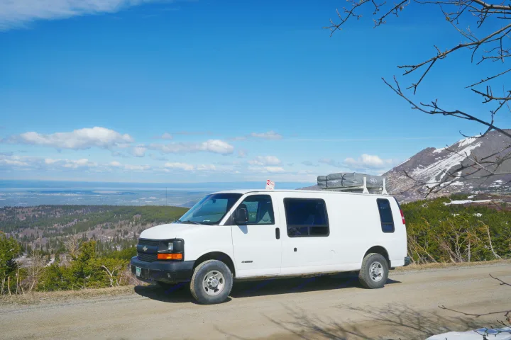 White rv rental van with rooftop tent parked on a mountain road, overlooking a vast forest and distant water under blue sky.. Chevrolet Other 2006