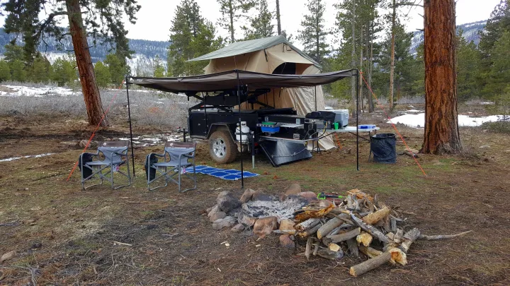 Adventure-ready RV rental: an overland camper trailer with rooftop tent, awning, pull-out kitchen, and fire pit in a snowy forest camp.. Insane Custom Trailers "Squatchy" 2022
