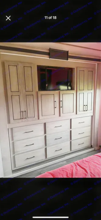RV rental bedroom with built-in storage: TV, light gray cabinets, and drawers. Pink bedding visible.. Heartland RVs Big Country 2021