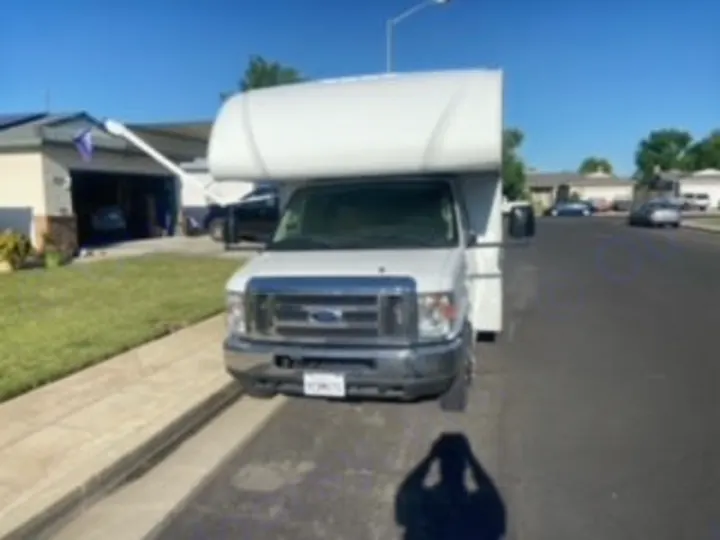 Front view of a white Class C Ford RV rental parked roadside on a sunny day. This recreational vehicle is ready for your trip.. Thor Four Winds 2020
