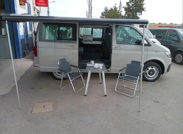RV rental: Grey camper van with extended awning, outdoor chairs, and table for comfortable travel living.. Volkswagen California Beach Camper 2.0 TDI 2023