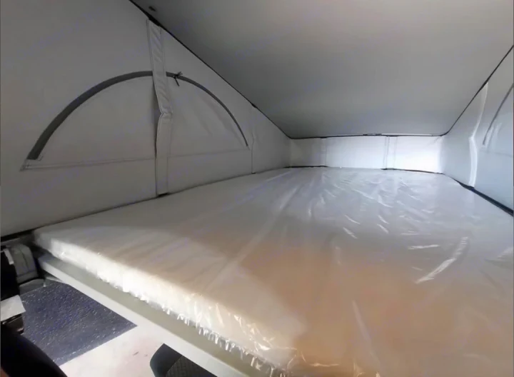 Inside an RV rental: a bright pop-top sleeping area with a new, plastic-wrapped mattress, ready for rest.. Volkswagen California Beach Camper 2.0 TDI 2023