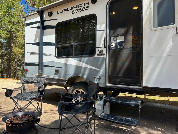 RV rental with a cozy outdoor camping setup: chairs, fire pit, and propane tank, nestled among trees for relaxation.. Starcraft Launch Outfitter Extreme 2018