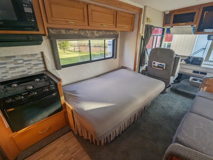 RV rental interior featuring a kitchen with microwave and stove, a convertible bed, and front driving area.. Itasca Sunova 2006