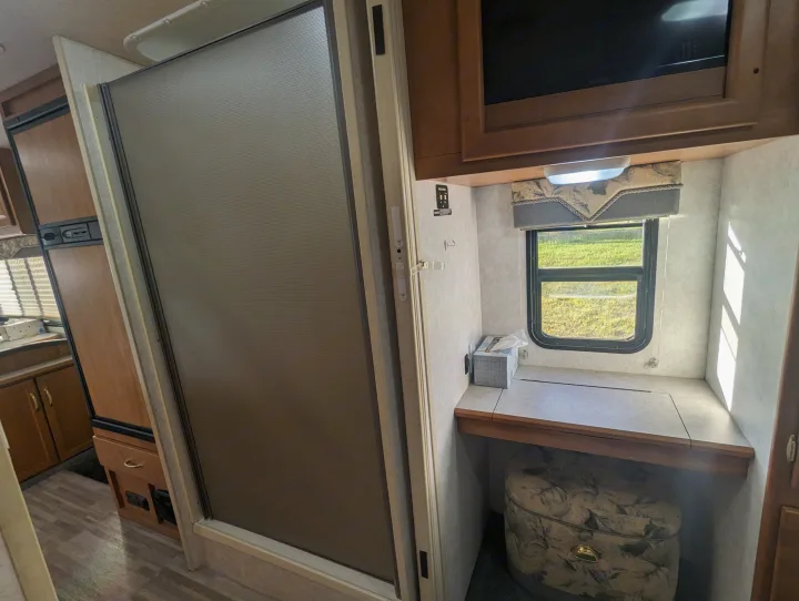 RV rental interior with a shower, fridge, and a built-in desk/vanity near a window, offering compact comfort.. Itasca Sunova 2006