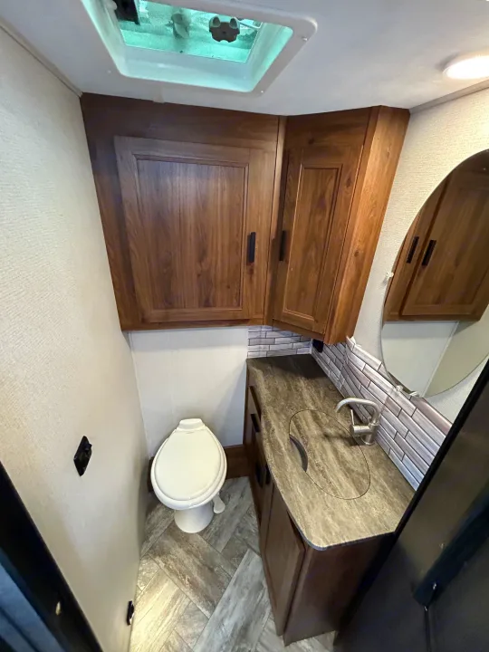 Explore this RV rental's compact bathroom, featuring a toilet, vanity with sink, and wooden overhead cabinets for convenience.. Forest River Forester 2021