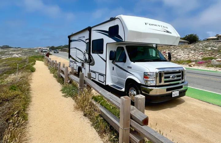 A white Forest River Forester RV rental parked by a scenic California coastal road and walking path under a blue sky.. Forest River Forester 2021