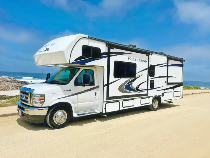 Forester Class C RV rental, white with black graphics, parked on a sandy road by the ocean.. Forest River Forester 2021