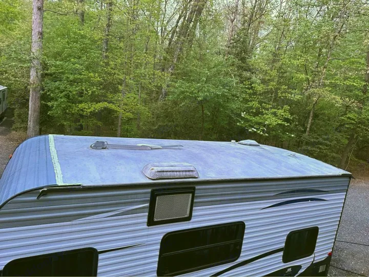 An RV rental parked outdoors, showing its roof with vents & a side view against lush forest trees.. Keystone RV Summerland Mini 2017
