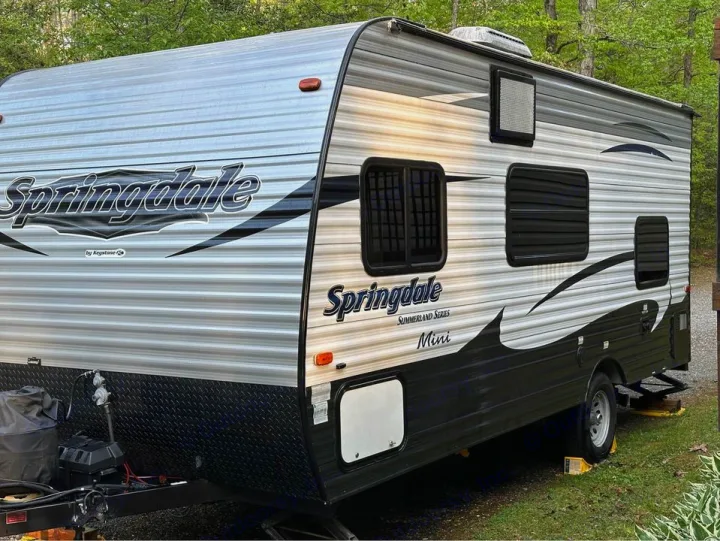 Springdale Summerland Mini RV rental, grey and black, parked with leveling blocks at a wooded campsite, ideal for travel.. Keystone RV Summerland Mini 2017