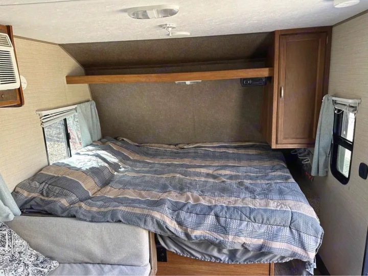 Spacious RV rental bedroom featuring a large bed with striped comforter, windows, AC, and storage. Ideal for travel comfort.. Keystone RV Summerland Mini 2017
