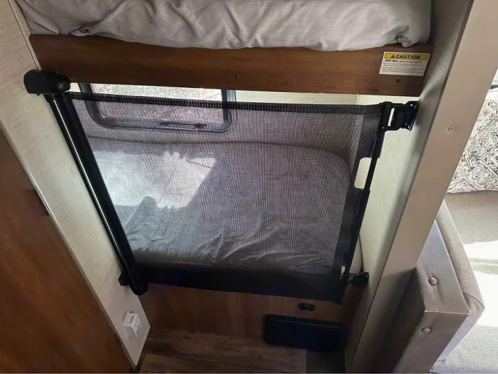 RV rental: a bunk bed with a black mesh child safety gate secured, ensuring safe travel for families.. Keystone RV Summerland Mini 2017