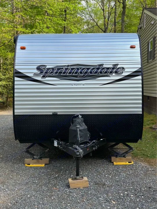 Front view of a Springdale travel trailer, ideal for an RV rental. Parked on gravel with stabilizers, ready for your camping trip.. Keystone RV Summerland Mini 2017