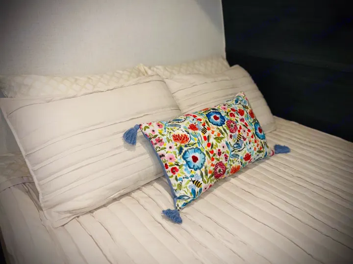 Cozy RV rental bedroom with white pleated bedding and a vibrant floral lumbar pillow.. Keystone RV Springdale Mini 1800BH 2024