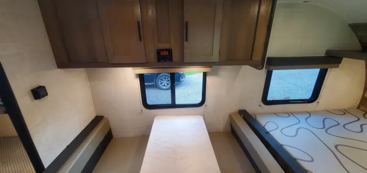 RV rental interior with a dinette, central table, overhead cabinets, and a patterned bed.. Gulf Stream Trailmaster 2022