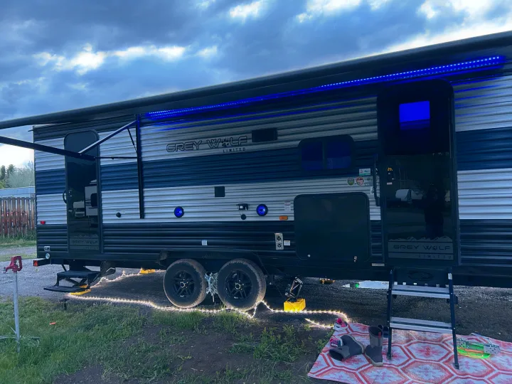 Evening RV rental setup: A Grey Wolf RV illuminated by blue LED awning and ground string lights, creating a cozy campsite.. Forest River Cherokee Grey Wolf 2022