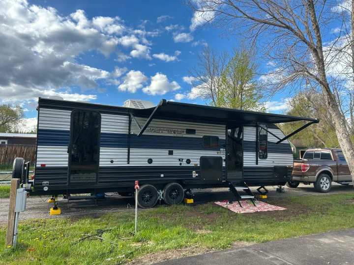 Grey Wolf travel trailer RV rental set up at a campsite with an extended awning and a brown pickup truck.. Forest River Cherokee Grey Wolf 2022