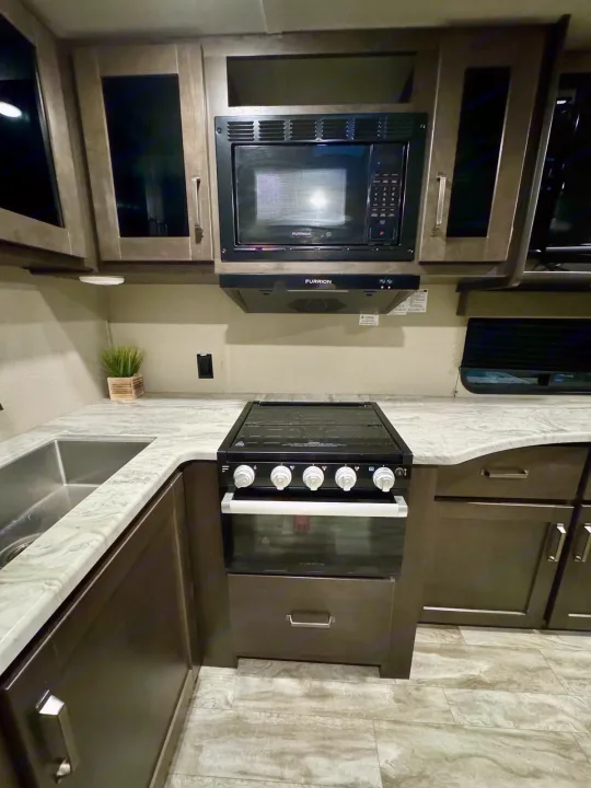 Experience comfort in this well-equipped rv rental kitchen featuring a sink, stove, microwave, and cabinetry for your travels.. Grand Design Transcend Xplor 2022