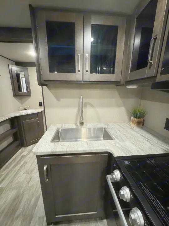 Modern RV rental interior showing a compact kitchen with sink, stove, cabinets, and an adjacent bathroom vanity.. Grand Design Transcend Xplor 2022