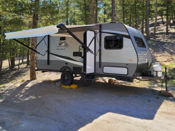 This Jay Flight travel trailer RV rental is set up in a pine forest campsite, ready for adventure.. Jayco Jay Flight SLX Baja Edition 2021