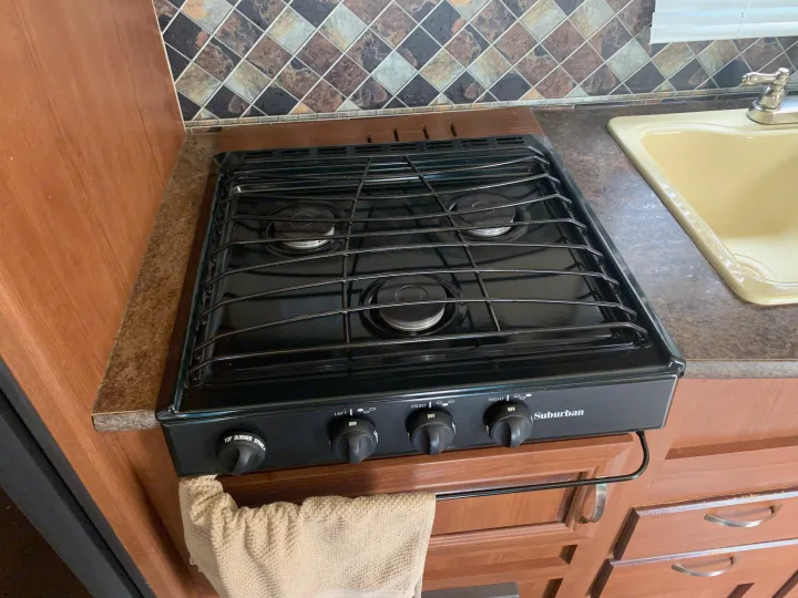 Inside this RV rental, find a functional kitchen with a Suburban 3-burner gas cooktop, sink, and tiled backsplash.. Forest River Salem Cruise Lite 2015