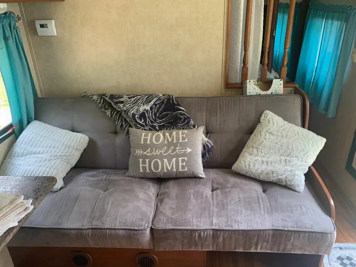 Cozy RV rental interior: grey futon, "Home Sweet Home" pillow, and blue curtains in the living space.. Forest River Salem Cruise Lite 2015