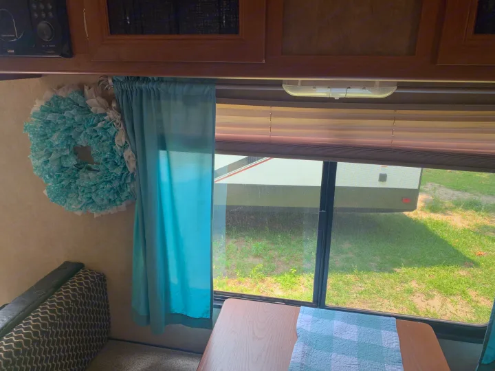 Inside an RV rental: a bright dining area with teal accents, looking out to green grass & another RV. Ideal for travel.. Forest River Salem Cruise Lite 2015