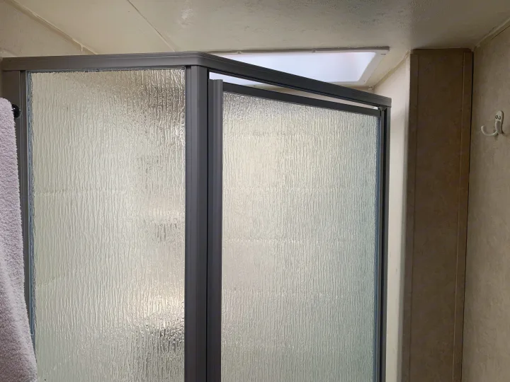 Inside an RV rental shower featuring textured frosted glass doors, an overhead skylight, and wall hooks.. Forest River Salem Cruise Lite 2015