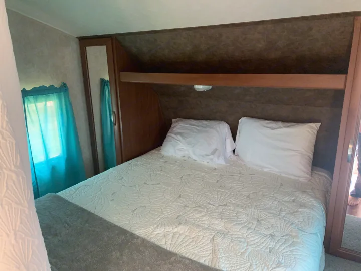 Comfortable RV rental bedroom with a white shell-patterned comforter, storage, and blue curtains.. Forest River Salem Cruise Lite 2015