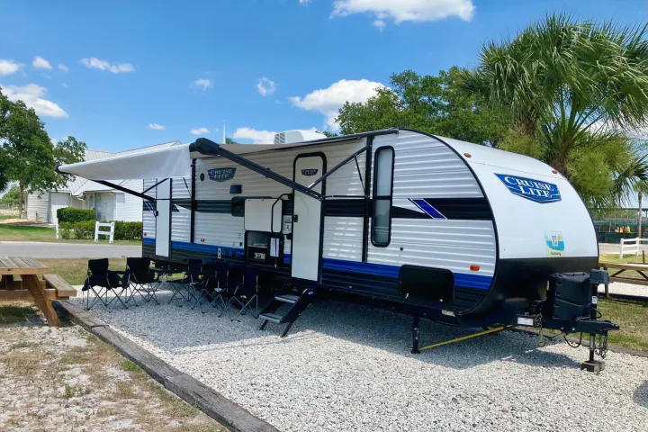 Cruise Lite RV rental ready for camping! This white and blue travel trailer is set up with awning and chairs at a sunny site.. Forest River Salem Cruise Lite 2023