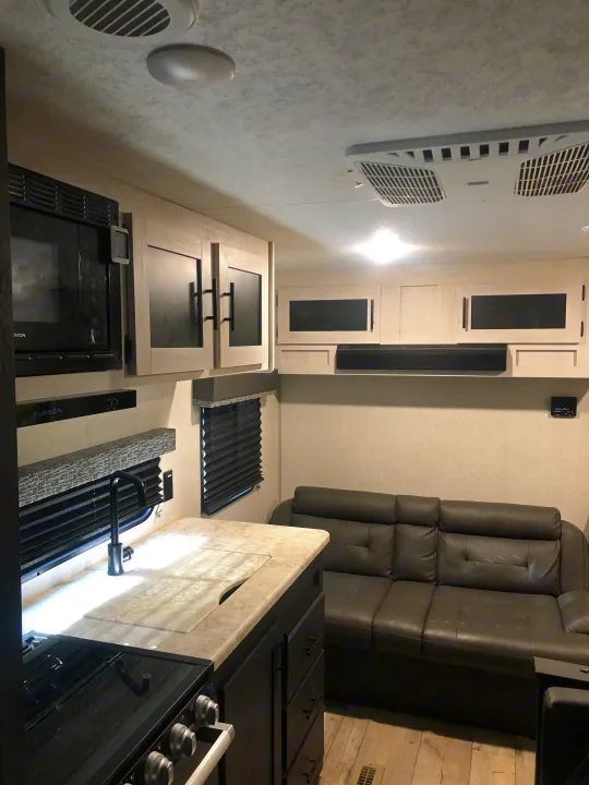 Inside a comfortable RV rental: A well-appointed kitchen with appliances & sink, and a relaxing living area featuring a dark sofa.. KZ Sportsman SE 2022
