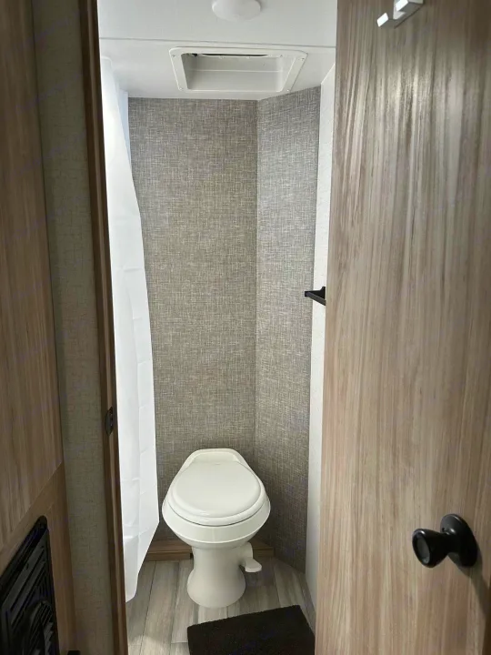 RV rental bathroom showing a compact white toilet, shower curtain, and textured walls. Ideal for mobile travel comfort.. Winnebago Micro Minnie 2022