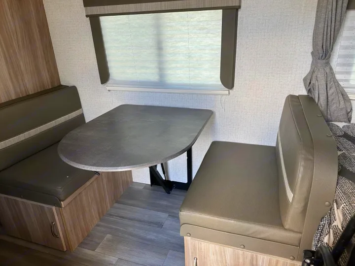 Inside an rv rental: A modern dinette with gray upholstered benches, a sturdy table, and a window with blinds.. Winnebago Micro Minnie 2022