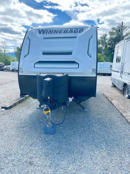 Front view of a white Winnebago travel trailer with hitch & propane tanks on a gravel lot. Ideal for rv rental camping.. Winnebago Micro Minnie 2022