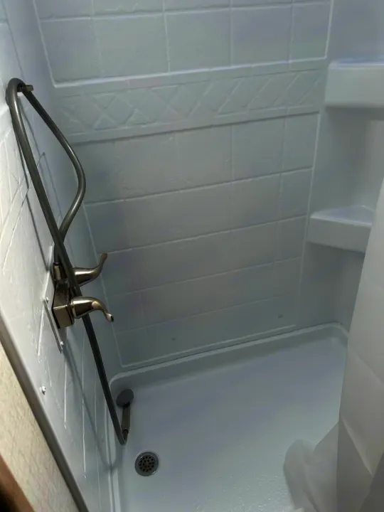 Bright white RV rental shower stall interior with adjustable head, faucets, textured walls & shelf.. Winnebago Micro Minnie 2022