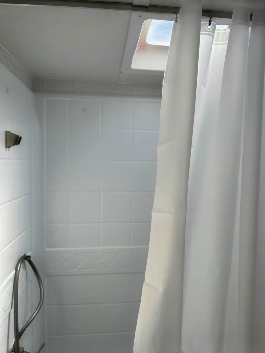 Clean RV rental shower featuring white tiled walls, a skylight, and a drawn white curtain. Ready for your travels!. Winnebago Micro Minnie 2022