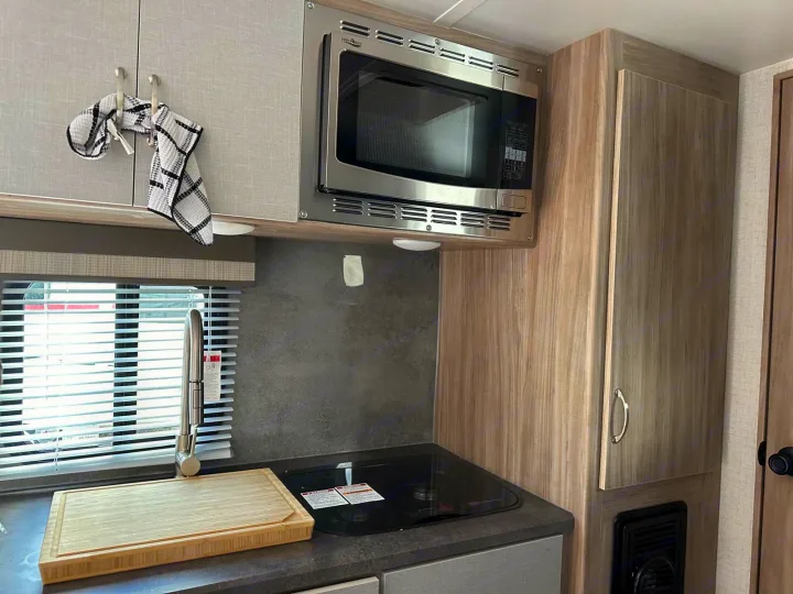 RV rental kitchen: stainless microwave, cooktop, sink, and light wood cabinets in a compact setup.. Winnebago Micro Minnie 2022