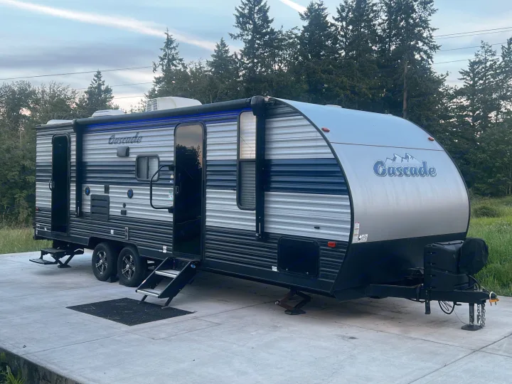This modern grey-and-black Cascade travel trailer, perfect for an rv rental, is set up on a concrete pad with steps down, ready for your trip.. Forest River Cherokee Grey Wolf 2021