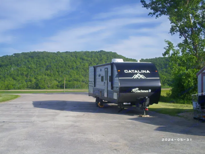 Coachmen Catalina RV rental parked on pavement, foreground. Lush green hills under blue sky in background.. COACHMAN CATALINA 261BHS 2024