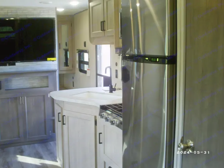Modern RV rental interior with light wood kitchen, stainless steel fridge, sink, stovetop, and large TV entertainment area.. COACHMAN CATALINA 261BHS 2024