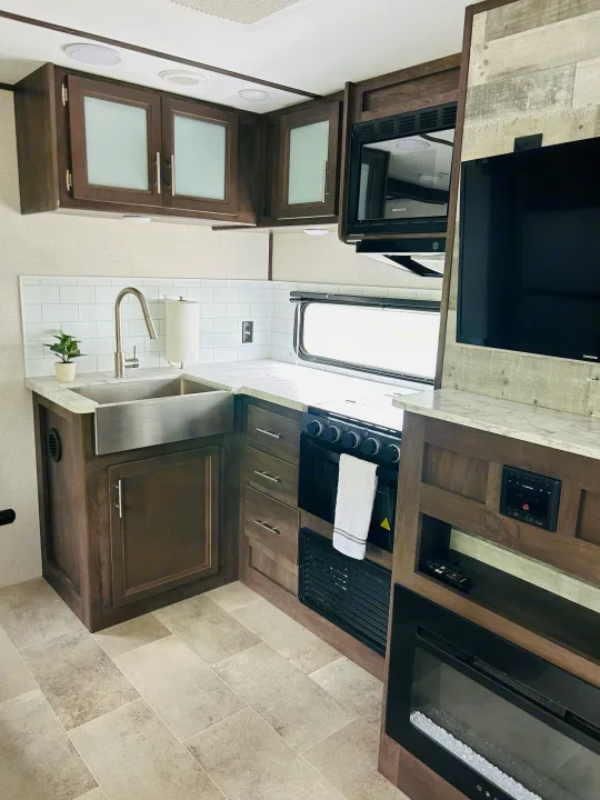 RV rental showcases a modern kitchen (farmhouse sink, microwave, stove) and living area (TV, electric fireplace, wood accents).. Dutchmen Coleman Light 2021