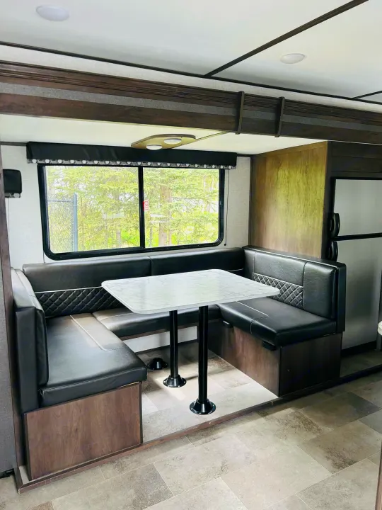 This **rv rental** features a clean, modern dinette. Black upholstered booth seating, a light table, and large windows create a bright space.. Dutchmen Coleman Light 2021