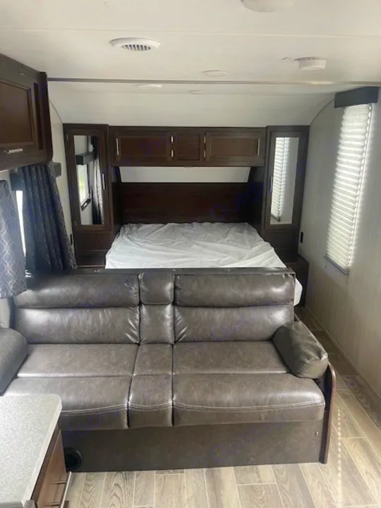 An RV rental's cozy interior, featuring a bed with overhead cabinets, mirrored wardrobes, and a sofa.. CHEROKEE GREY WOLF 26DJSE 2021